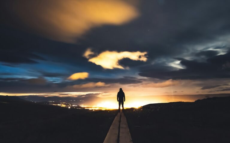 Person standing on a path overlooking a sunrise over a city skyline.
