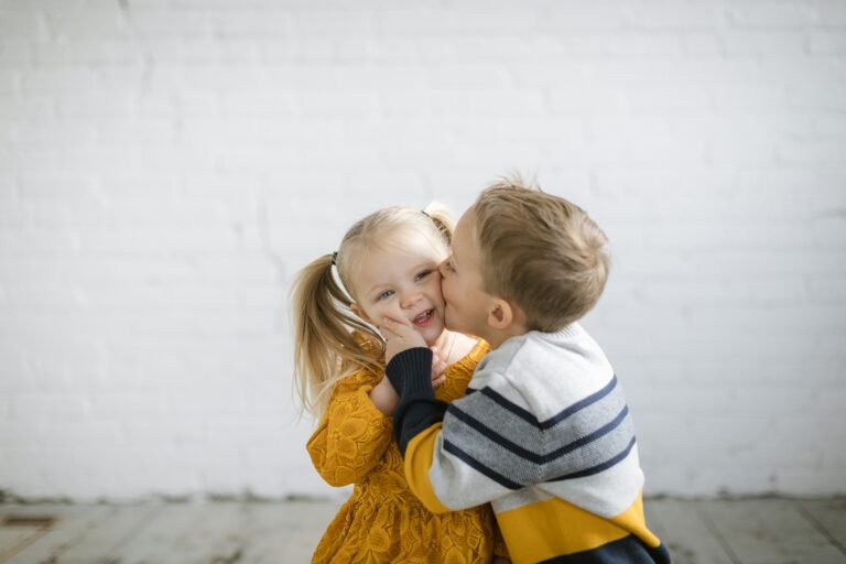 Children sharing a kiss outdoors, brother and sister smiling together.