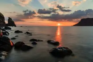 Sunset over rocks and calm sea with warm orange glow.