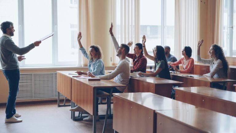 Classroom with students raising hands during a lecture and a teacher at the front.