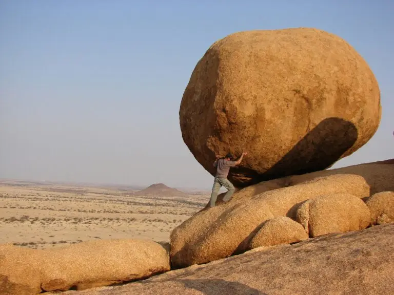 Person balancing a large rock on a desert rock formation.