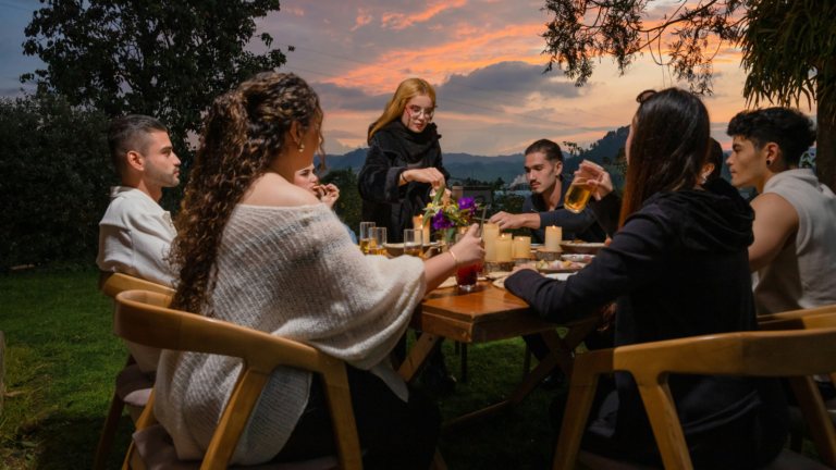 People gathered around a table outdoors at sunset sharing a meal and drinks.